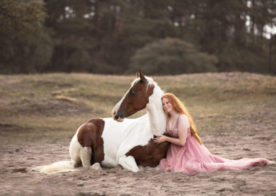 Rothaarige sitzt mit Pferd auf Erde